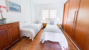 Een hotelkamer met twee bedden, een houten garderobe, een schilderij en een raam met zonwering.