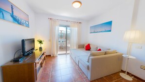 Een woonkamer met een televisie, bank en lamp. Er hangt een schilderij aan de muur en er is een raam met gordijnen.