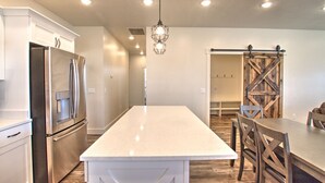 A modern kitchen with a central island, stainless steel appliances, and a rustic wooden door. - Blue Bear Bungalow - Pool Access and only One Block From The Lake! (Garden City)