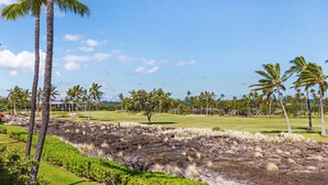 A golf course with a rocky outcrop, palm trees, and a clear blue sky.