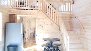 A wooden cabin interior with a central staircase, a dining area, and a kitchen. - King of Hearts.  Secluded Hocking Hills cabin! (Rockbridge)