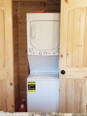 Ein kleiner Waschraum mit einer Frontlader-Waschmaschine und einem Trockner, Holzwänden und einer Tür.