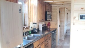 Eine kleine Küche mit Holzausstattung, einem Edelstahlkühlschrank, einer Mikrowelle und einem Geschirrspüler.