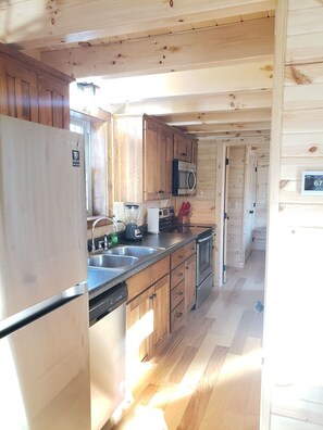 A compact kitchen with wooden cabinets, a stainless steel refrigerator, a microwave, and a dishwasher.