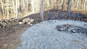 A forested area with a gravel fire pit surrounded by metal chairs. - King of Hearts. Secluded Hocking Hills cabin! (Rockbridge)