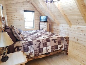 Ein Schlafzimmer einer Holzhütte mit einem Bett, einem Nachttisch, einer Lampe und einem Fenster.