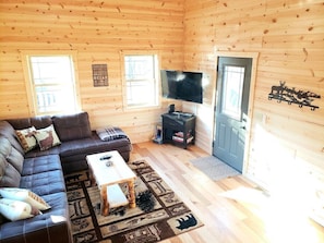 Un interior de cabaña con sofá, mesa de centro, televisor y chimenea.