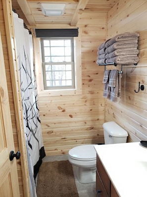 Un baño pequeño con paneles de madera, un inodoro, una ventana y un perchero para toallas.