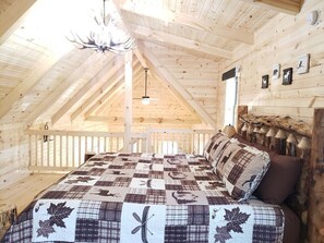 Un dormitorio acogedor en el ático, con techo de madera, colcha acolchada y ventilador de techo.