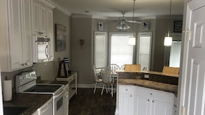 Une cuisine avec des meubles blancs, un fourneau et un ventilateur de plafond.