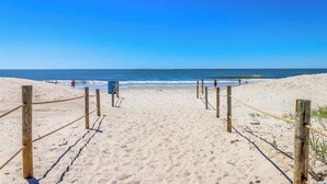Une plage de sable avec des poteaux en bois et des cordes, qui mènent à l’océan.