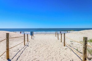 Une plage de sable avec des poteaux en bois et des cordes, qui mènent à l’océan.