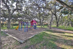 A playground with a swing set, slide, and climbing structure surrounded by trees. - Waterfront Escape | Private Beach + 2 Pools (St. Petersburg)