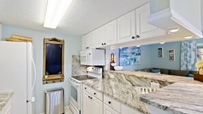 Una cocina moderna con armarios blancos, encimera de mármol y microondas integrado.