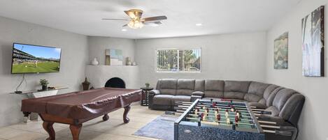 A living room with a pool table, foosball table, and a large sofa.