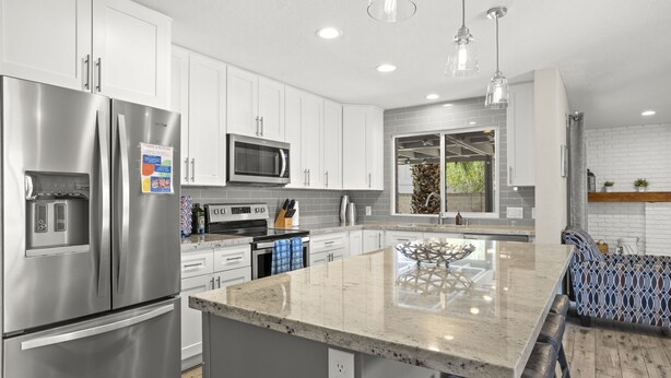 Una cocina moderna con gabinetes blancos, electrodomésticos de acero inoxidable y una isla central con asientos.