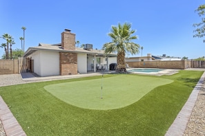 Un jardin avec un terrain d’entraînement au golf, une piscine et une maison dotée d’une terrasse.