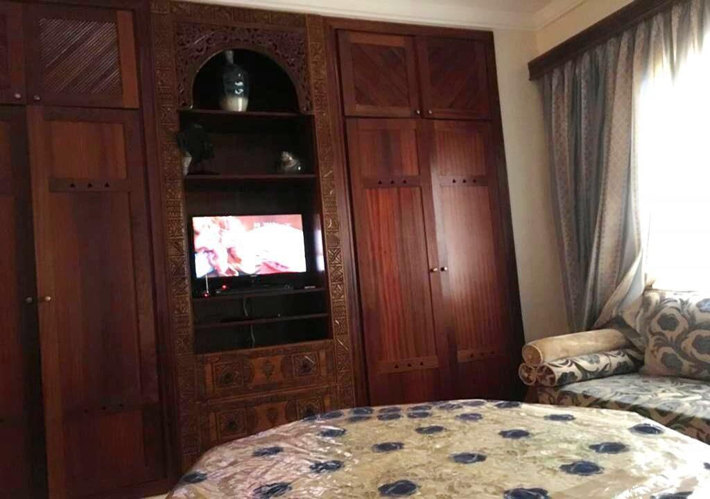 Ein Zimmer mit einem großen, hölzernen Schrank mit Regalen, einem Fernseher und einer gestreiften Bettdecke.