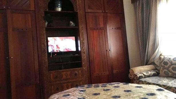 Ein Zimmer mit einem großen, hölzernen Schrank mit Regalen, einem Fernseher und einer gestreiften Bettdecke.