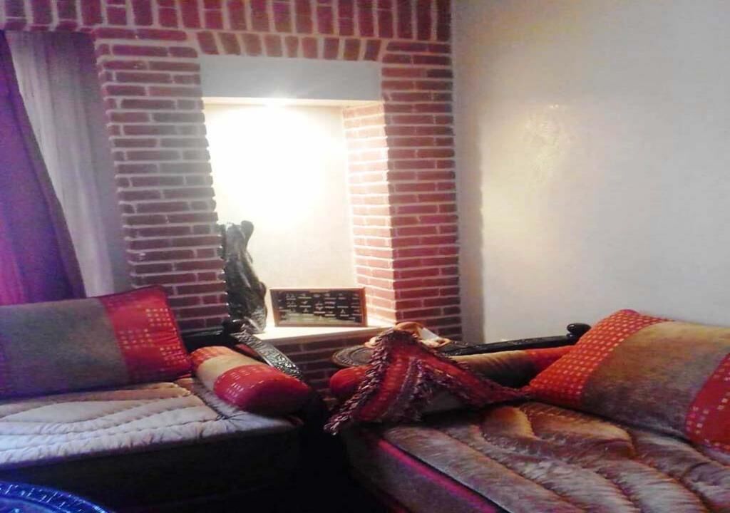 Ein Zimmer mit Kamin aus Ziegelsteinen, einer Couch mit roten und beigen Kissen sowie einem Fenster mit Blick nach draußen.