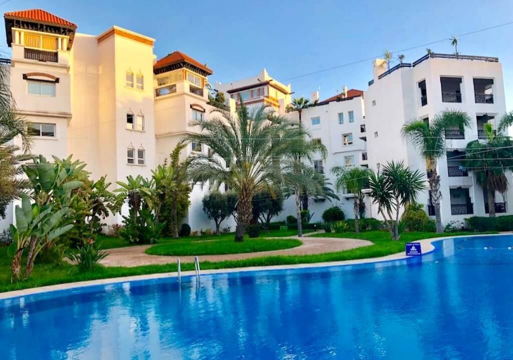 A swimming pool surrounded by lush greenery and white buildings with balconies.