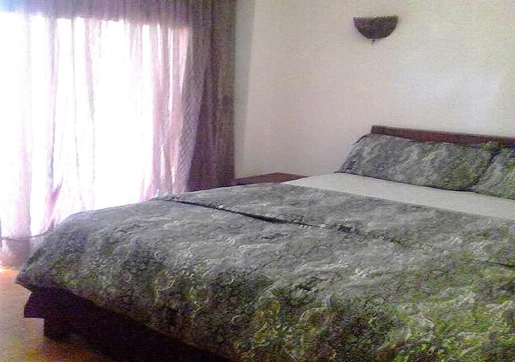 A bedroom with a bed, curtains, and a wall-mounted light fixture.