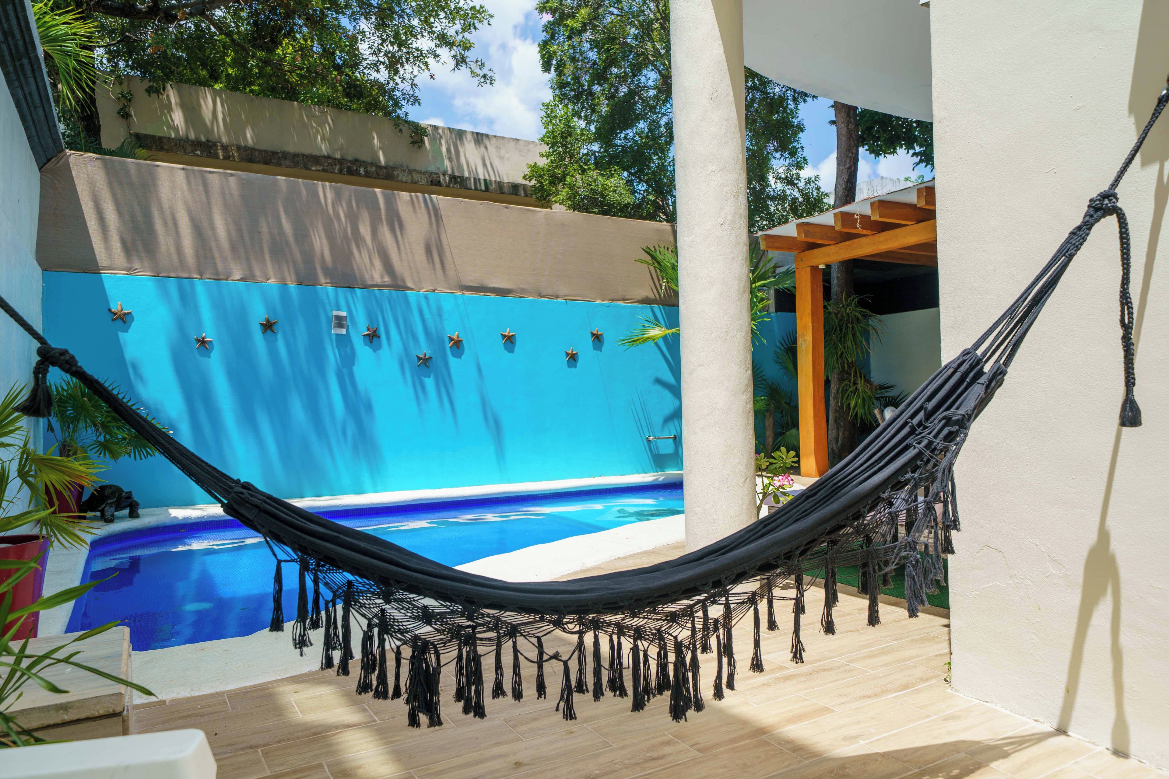 A hammock in a sunlit outdoor area with a pool and a blue wall.