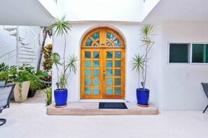 A white building with a wooden door, potted plants, and a spiral staircase.