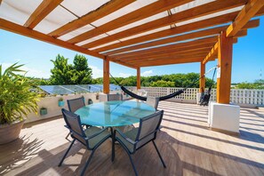 En overdækket udendørs terrasse med et glasbord og stole, solpaneler og udsigt til byens skyline.