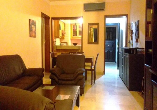 A living room with a sofa, armchair, and a dining area with a table and chairs.
