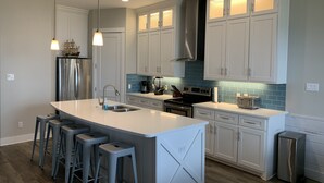 A modern kitchen with white cabinets, a stainless steel refrigerator, a central island with bar stools, and a blue-tiled backsplash. - HUGE 4BR/3BA! Pool, Beach & Boat Slip! 4 Car Garage  (Corpus Christi)