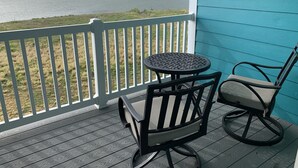 A wooden deck with a table and two chairs, overlooking a body of water and a distant shoreline.