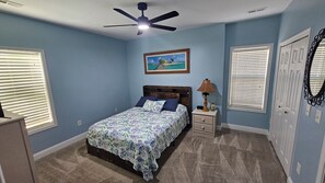 Een slaapkamer met een bed, nachtkastje, plafondventilator en een raam met jaloezieën.