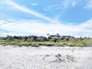 A beachfront property with multiple buildings, sandy beach, and sparse vegetation.