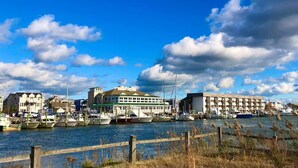 Uma marina com barcos atracados, um edifício com telhado verde e uma fileira de edifícios brancos com varandas.