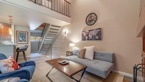 A spacious living room with a grey sofa, a wooden coffee table, and a staircase leading to an upper level. - Family Condo in Carnelian Woods (Carnelian Bay)