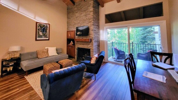 A cozy living room with a stone fireplace, a sofa, and a dining table with chairs. - Family Condo in Carnelian Woods (Carnelian Bay)