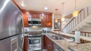 A modern kitchen with stainless steel appliances, wooden cabinets, granite countertops, and a tiled backsplash. - Family Condo in Carnelian Woods (Carnelian Bay)