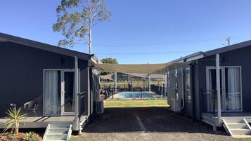 A modern building with a pool, outdoor seating, and a large tree.