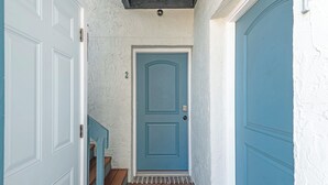 Un couloir avec une porte bleue, des murs blancs et un plancher en bois.