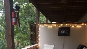 Een hottub op een houten terras met sfeerverlichting, twee stoelen en een bordje met de tekst 'PORCH'.