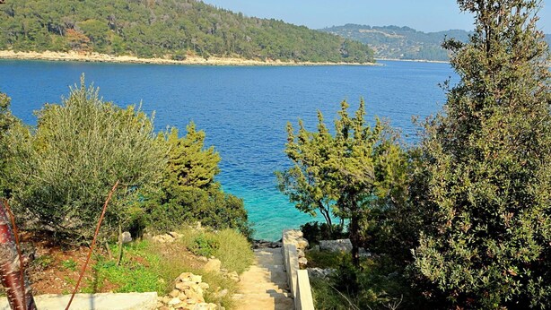A stone staircase leading to a coastal area with clear blue water and green trees.