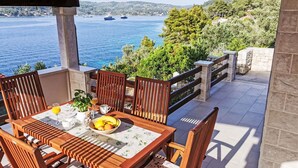 A wooden table with chairs and a bowl of fruit on a balcony overlooking a body of water and greenery.