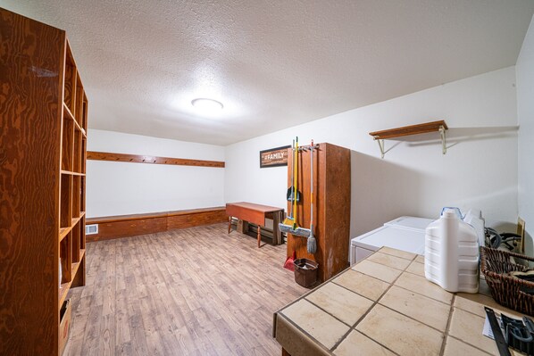 A room with wooden flooring, a wooden bookshelf, a bench, a broom, a bucket, a milk jug, and a basket. - Aspen House (Crested Butte)
