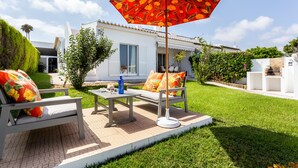 A patio with a table and chairs, a large umbrella, and a white building in the background. - CoolHouses Algarve Lagos | Casa Evasion (Lagos)