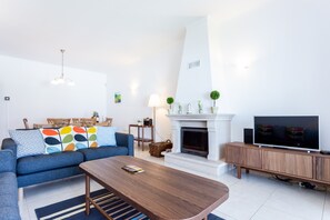 A modern living room with a sofa, coffee table, TV, fireplace, and a dining area with chairs and a table.