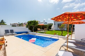 Une piscine avec des chaises longues et un parasol rouge.