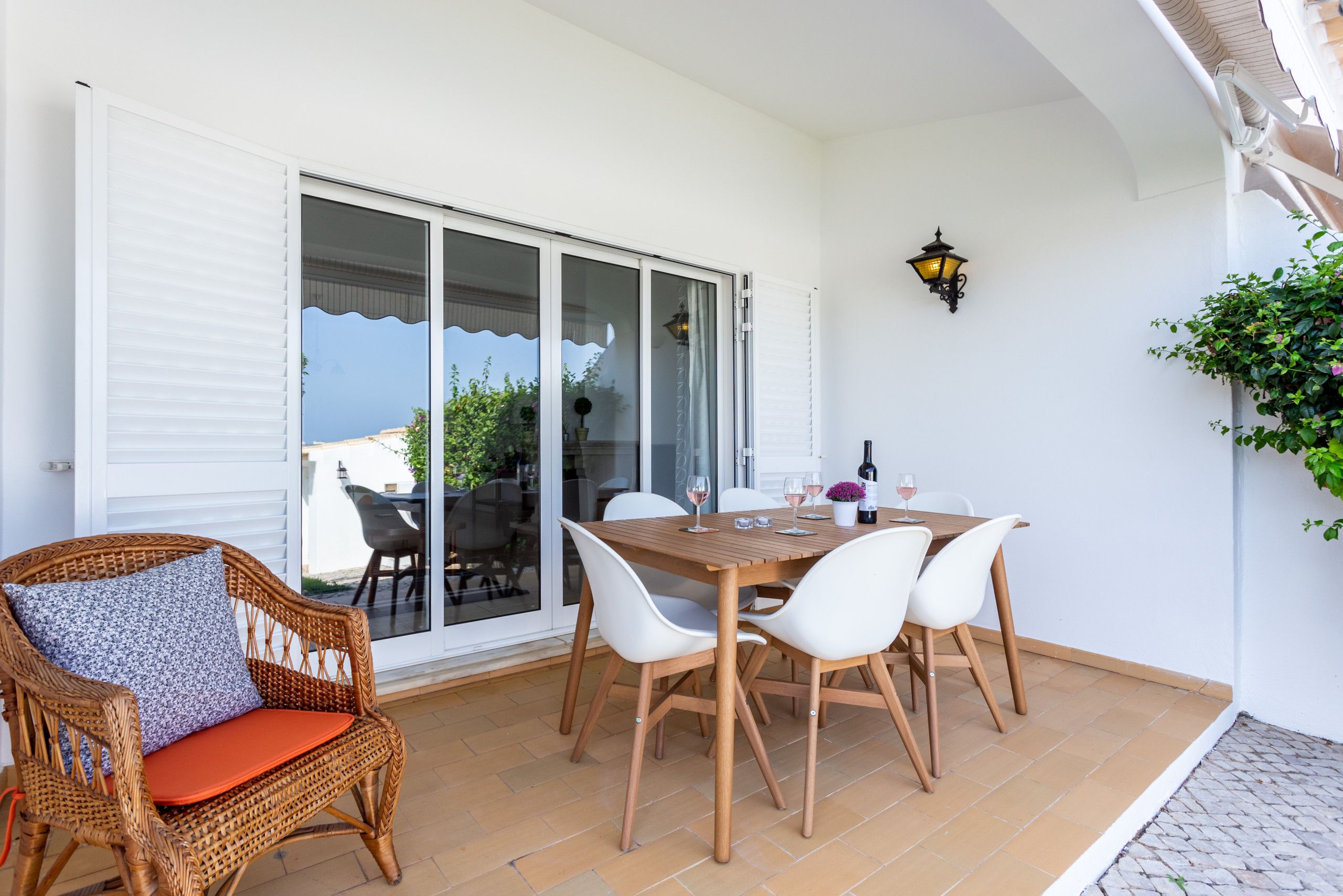 A patio with a table set for dining, chairs, a wicker chair with a cushion, and a potted plant.