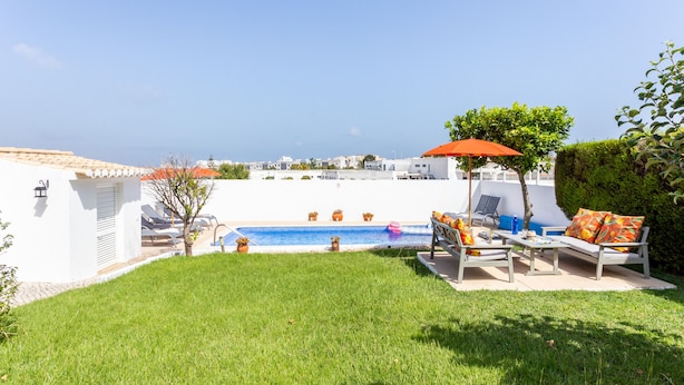 A pool area with lounge chairs and umbrellas, surrounded by a well-maintained lawn and a view of the sea. - CoolHouses Algarve Lagos | Casa Evasion (Lagos)