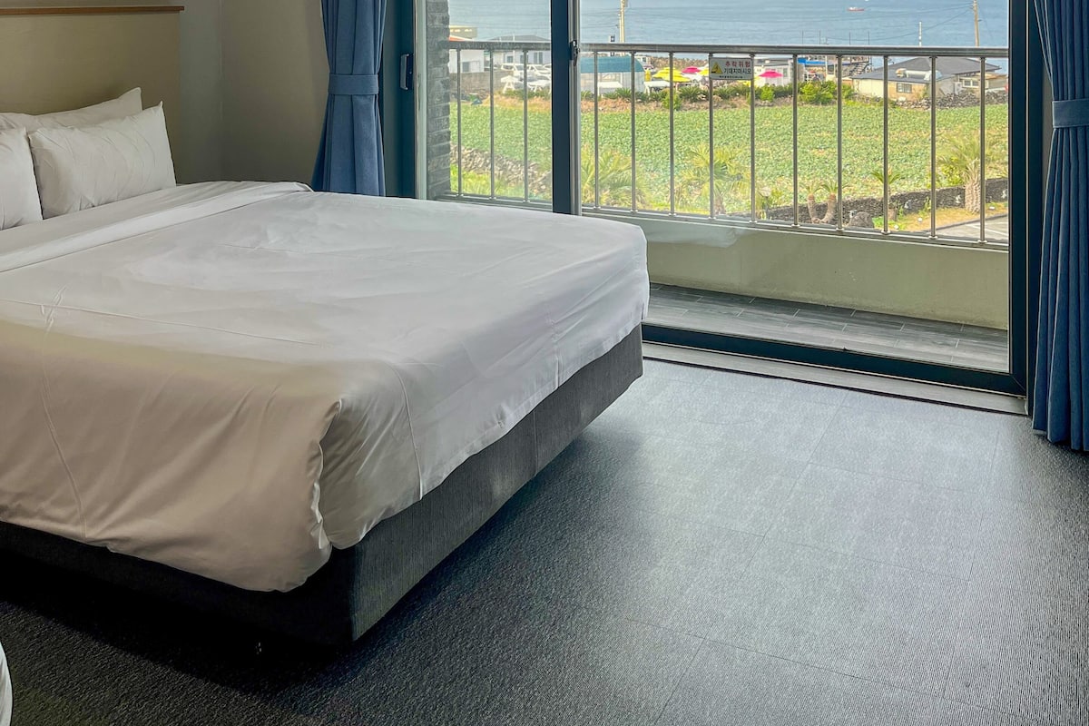 A hotel room with a large bed, a view of the sea, and a balcony with a railing.